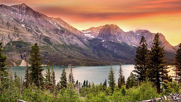 A landscape of greenery, a lake, and a mountain range under a technicolor sky. 