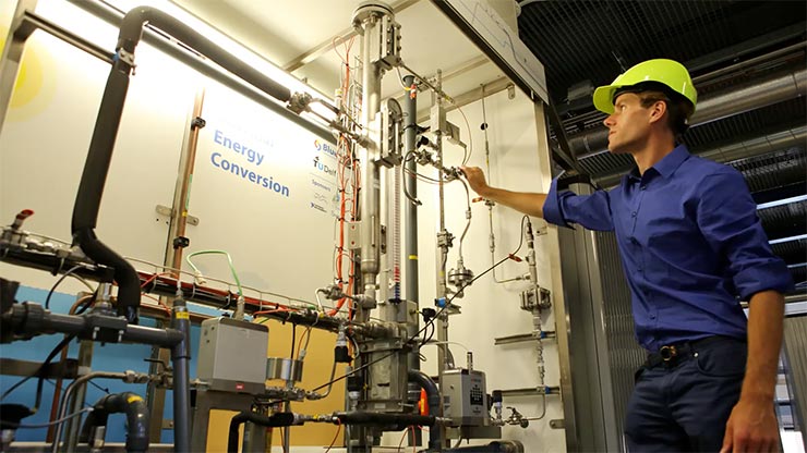 A person in a yellow hard hat tinkers with a piece of equipment associated with energy conversion.