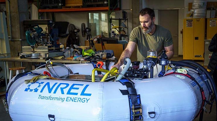 A person in a garage tinkering with a large white flotation device branded with a blue and green logo