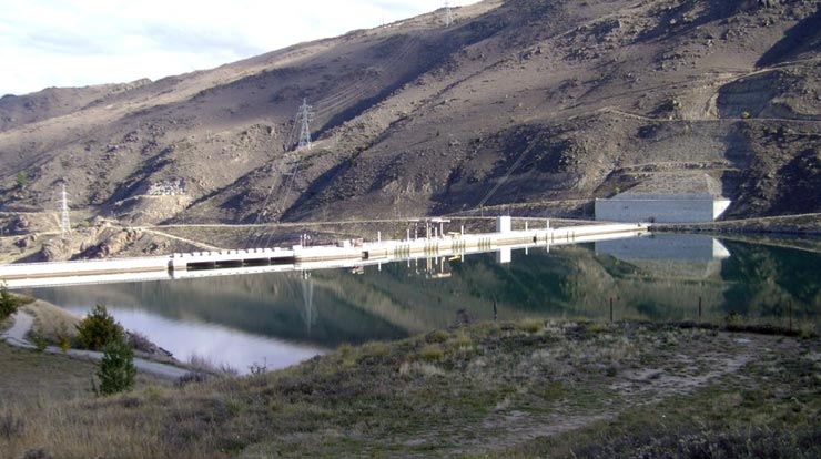A long white dam across a body of water with mountains in the background