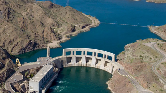 An overhead view of a large dam between two bodies of water and two mountains