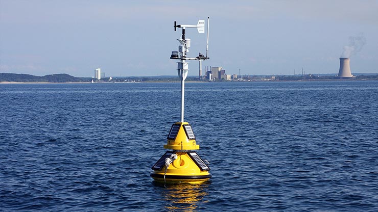 A yellow buoy floating in the ocean with data-collecting technologies attached.