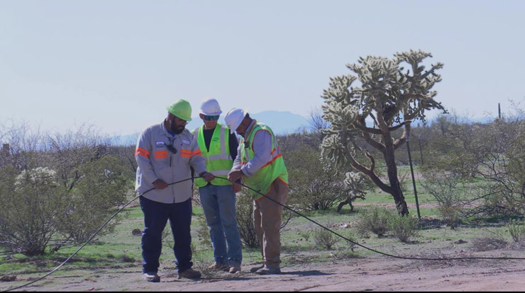 Three people wearing hard hats and neon workwear hold a cable in an arid-like landscape