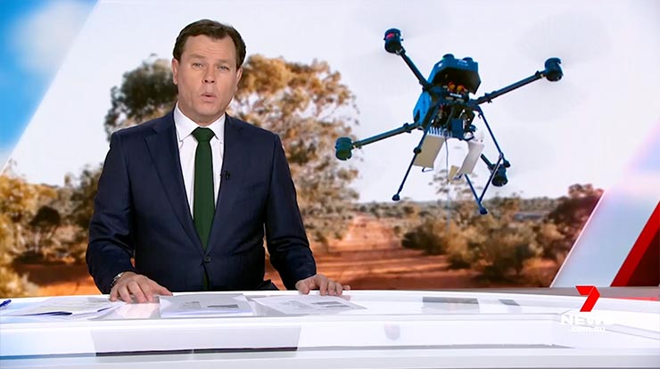 A person in a suit sits at a newscaster desk with a drone in the background image
