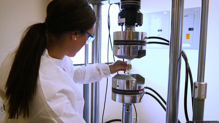 A person facing away from the camera wearing safety glasses and working on a silver device
