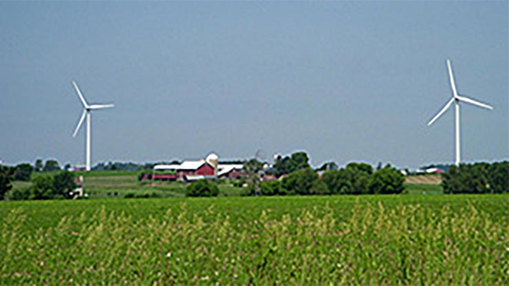 Two wind turbines along the horizon, where green farmland meets the sky.