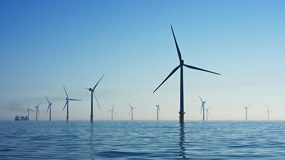 An illustration of three offshore wind turbines, a boat, and land in the background.
