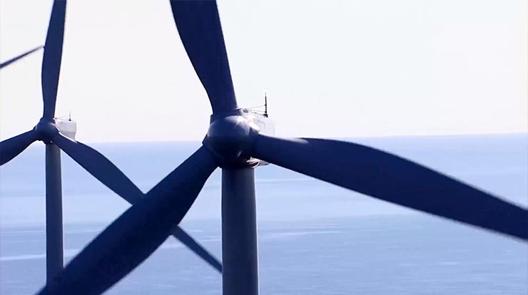Enlarged view of two offshore wind turbines with ocean in the background. 